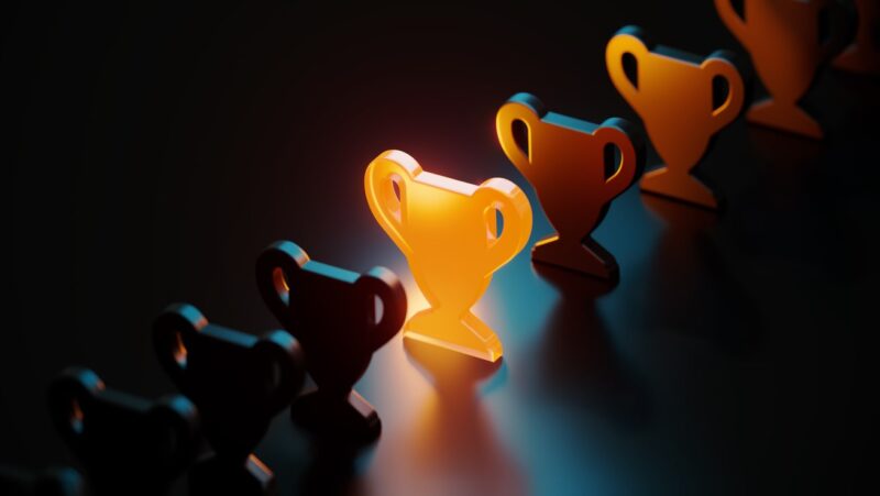 Trophy symbol glowing amid black trophy symbols on black background.