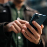 Close-up hands of unrecognizable man holding and using smartphone standing on city street