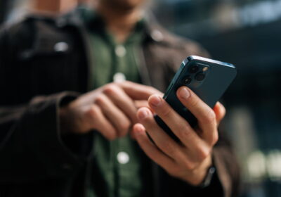 Close-up hands of unrecognizable man holding and using smartphone standing on city street